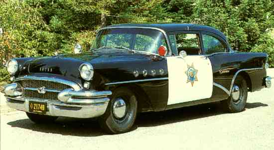 Black and white police car, looks like a 1956 Buick Century, parked outside