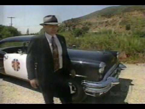 1991 Ford Crown Victoria - A man in a suit stands beside a black 1956 Buick Century, which has a white door with a red star emblem.