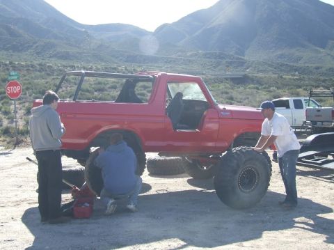 1978 Ford Bronco - People are working on the tires of a red 1978 Ford Bronco outdoors.