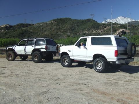 1978 Ford Bronco - Two SUVs are parked on a dirt road with mountains in the background.
