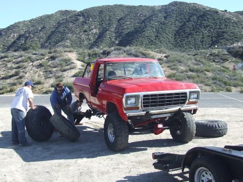 1978 Ford Bronco - A red 1978 Ford Bronco is being worked on by several people, with one tire removed and another nearby.