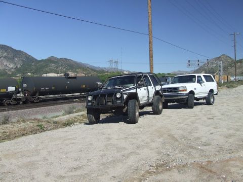 1978 Ford Bronco - Two SUVs are parked on a dirt road beside a train track with mountains in the background.