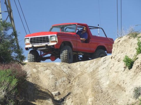 1978 Ford Bronco - A red 1978 Ford Bronco navigates a steep dirt incline with a driver visible inside.