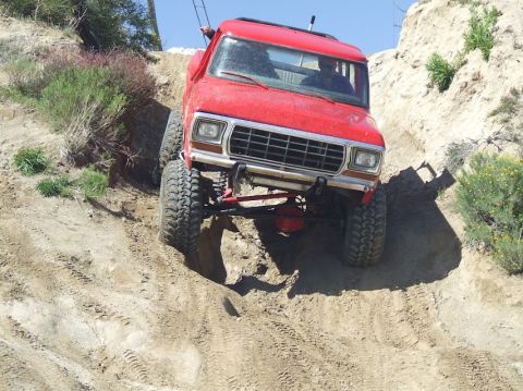 1978 Ford Bronco - This red Ford F-Series truck is navigating a steep, sandy incline with large off-road tires.