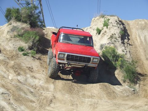 1978 Ford Bronco - A red off-road vehicle navigates a steep dirt incline under a clear blue sky.