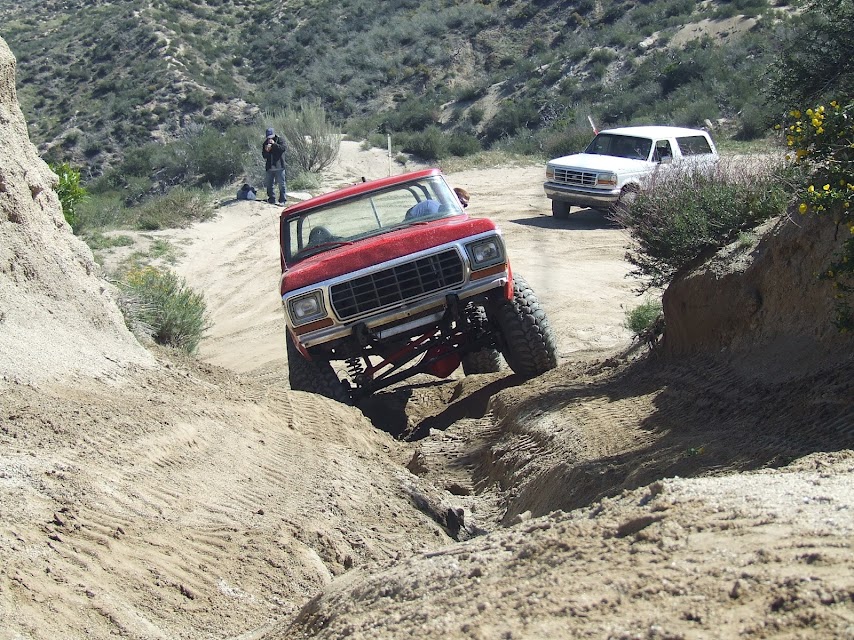 Red 1978 Ford Bronco descending a dirt trail, white Ford Bronco in background