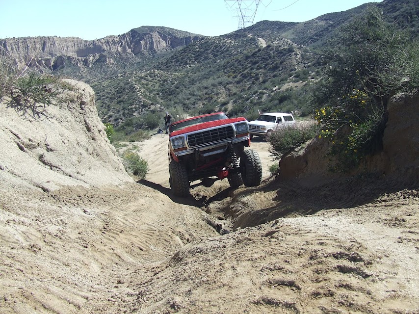 red SUV going down a steep dirt path, white SUV behind it