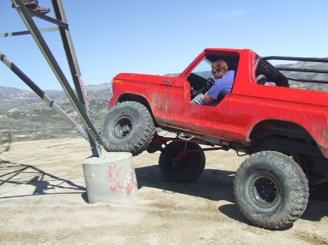 1978 Ford Bronco - A red 1978 Ford Bronco is shown off-roading, with one wheel on a concrete structure.