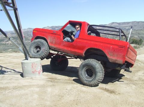 1978 Ford Bronco - A red 1978 Ford Bronco is shown off-roading, with its front tire resting on a concrete obstacle.