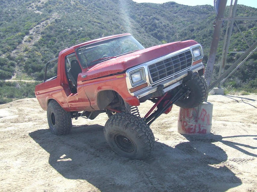 Red 1978 Ford Bronco with lifted suspension on a rocky incline