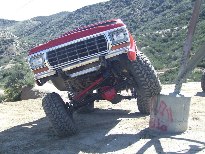 Red 1978 Ford Bronco with lifted suspension, front wheel on concrete obstacle