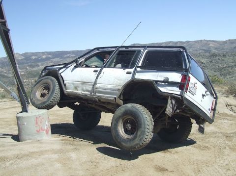 1978 Ford Bronco - Modified SUV with a roll cage and oversized tires navigates an obstacle on a dirt terrain.