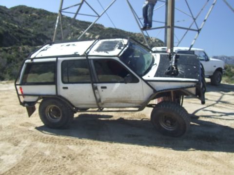 1978 Ford Bronco - A heavily modified white SUV with a roll cage sits parked outdoors next to another white vehicle.