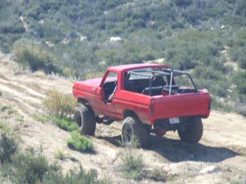 1978 Ford Bronco - A red 1978 Ford Bronco navigates a dusty off-road path with a roll cage installed.