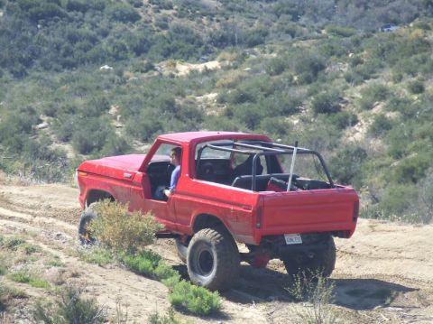 1978 Ford Bronco - This red 1978 Ford Bronco is captured navigating a dirt trail with its roll cage visible.