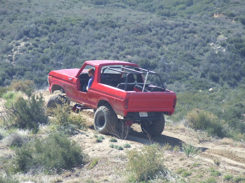 Red 1978 Ford Bronco with roll cage climbing a dirt hill