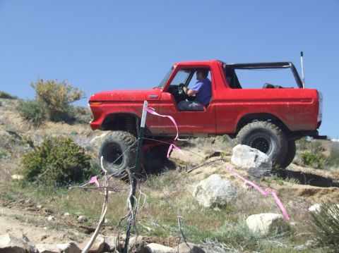 1978 Ford Bronco - A red 1978 Ford Bronco is driven over a rocky, off-road course under a clear blue sky.