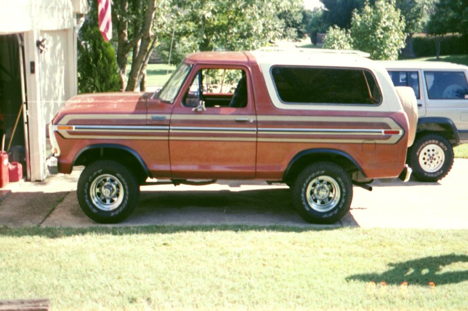 Side view of red and white lifted Ford Bronco SUV on chrome wheels in a driveway