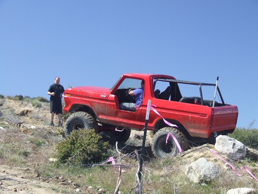 1978 Ford Bronco with roll cage on rocky terrain, driver inside, person standing beside it