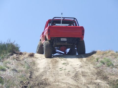 1978 Ford Bronco - This red pickup truck is equipped for off-road use, climbing a steep dirt incline under a clear blue sky.