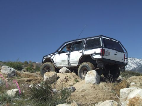 1978 Ford Bronco - A white SUV navigates a challenging rocky off-road course under a clear blue sky.
