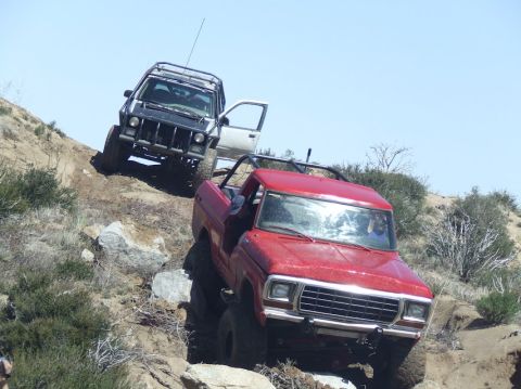 1978 Ford Bronco - Two off-road vehicles navigate a steep, rocky incline under a clear blue sky.