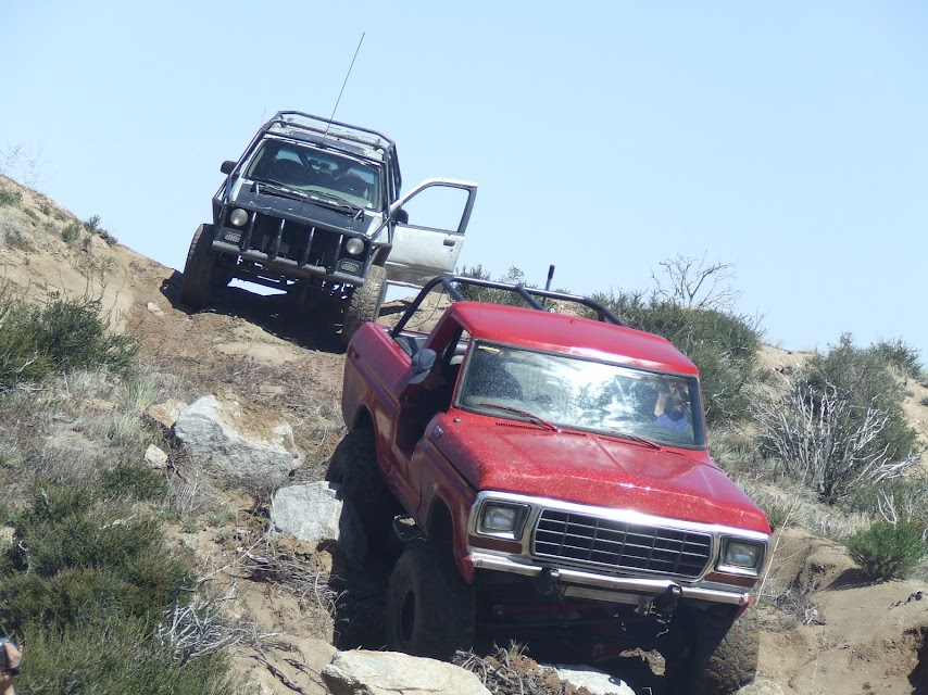 Red pickup truck with roll cage on rocky terrain, front grille visible