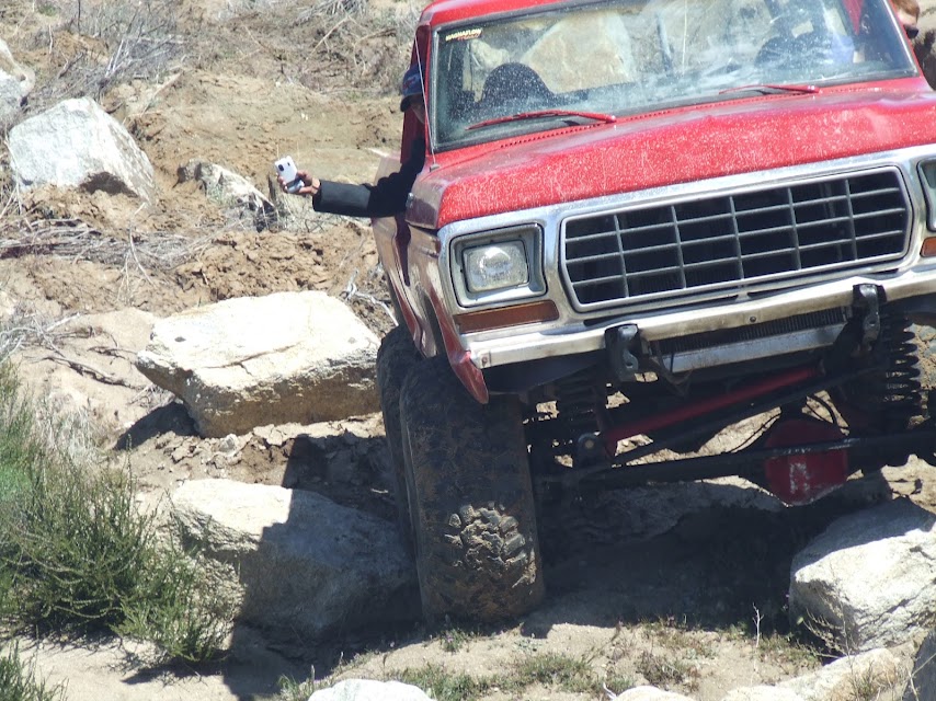 Red truck with lifted suspension navigating rocky terrain. Driver is holding a phone