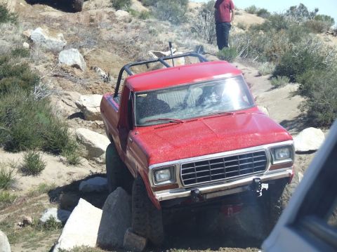1978 Ford Bronco - A red pickup truck with a roll cage is shown off-roading over rocks.