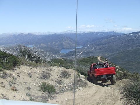 1978 Ford Bronco - A red pickup truck navigates a winding dirt road with a scenic mountain and lake vista.