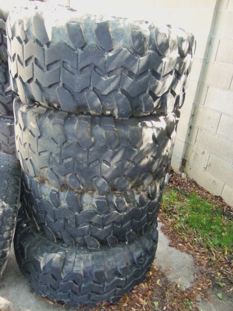1968 Ford Bronco - Several large, aggressive tread tires are stacked outdoors next to a wall.