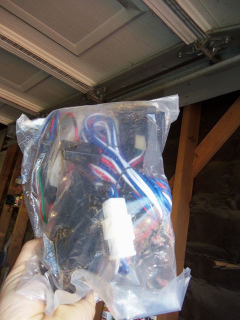 1968 Ford Bronco - A hand holds a new wiring harness, still in its plastic packaging, ready for installation.
