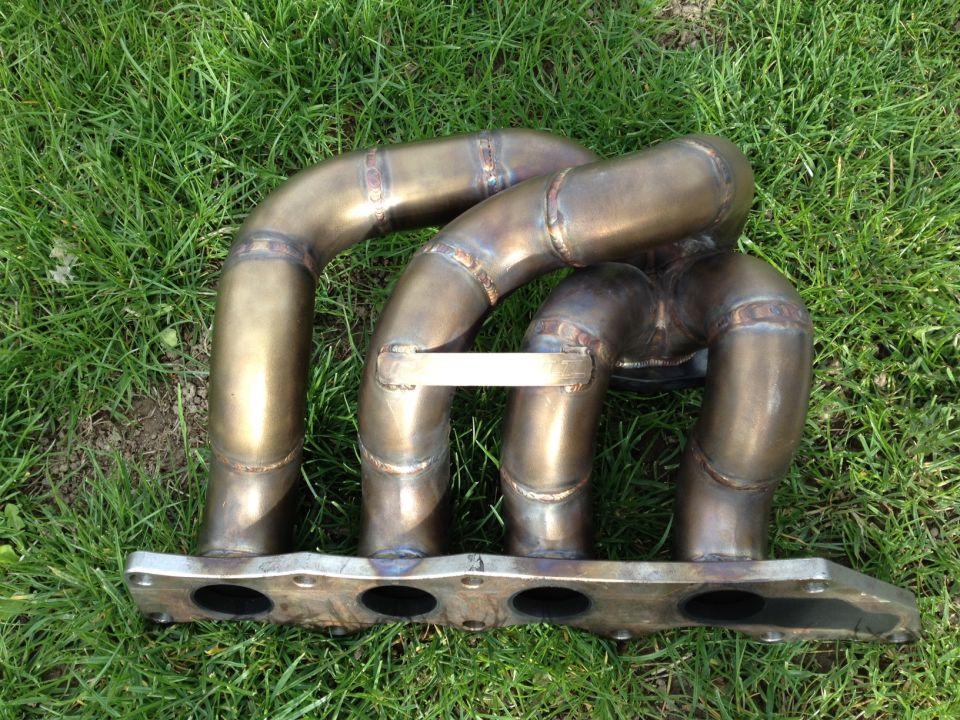 Custom exhaust manifold with four pipes merging into one, bolted to a flange with four openings