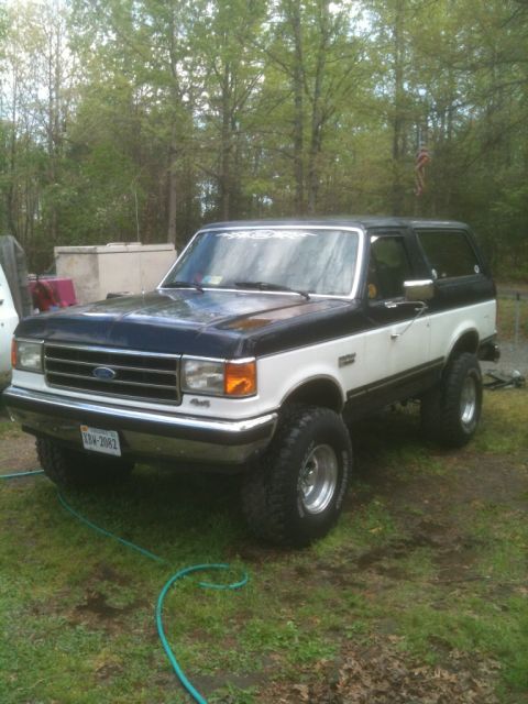 1989 Ford Bronco - This lifted Ford Bronco is parked outdoors on a grassy area, with trees forming the backdrop.