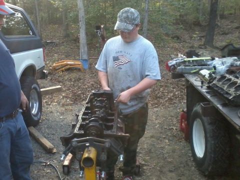 1989 Ford Bronco - A person works on an engine block while another person stands by a Ford Bronco in an outdoor setting.