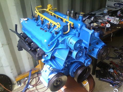 1989 Ford Bronco - A blue V8 engine is mounted on a stand, surrounded by tools and automotive supplies.