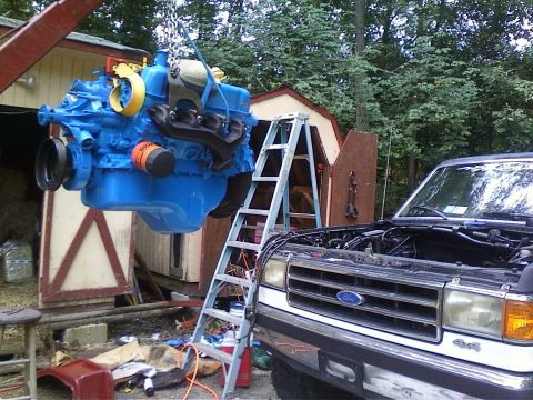 1989 Ford Bronco - A blue engine is being lowered into the engine bay of a Ford truck.