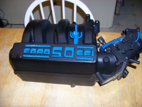 1989 Ford Bronco - A black Ford 5.0 EFI intake manifold with bright blue lettering is shown on a wooden surface.