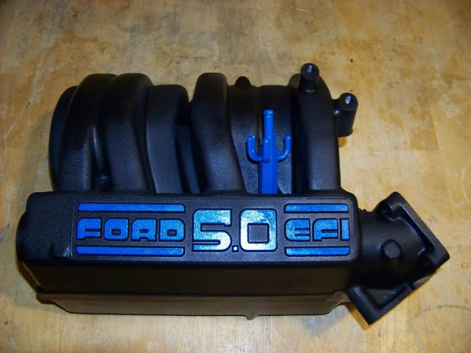 Black Ford 5.0 EFI intake manifold with blue lettering, resting on a wooden surface