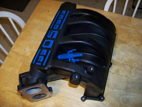1989 Ford Bronco - A black intake manifold with blue 'Ford 5.0 EFI' lettering is shown on a wooden table.