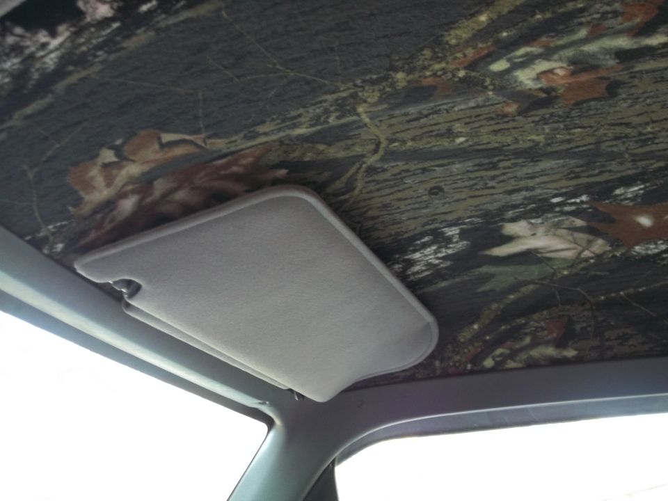 Interior view of a vehicle's headliner with camouflage pattern and a gray sun visor