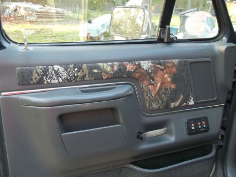 1989 Ford Bronco - The interior door panel of a vehicle features a camouflage accent strip above the armrest and a control panel for windows.