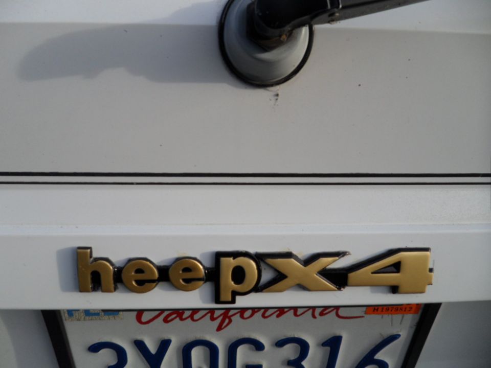 Gold 'Jeep 4x4' badge on white tailgate above California license plate