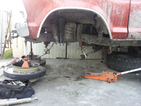 1978 Ford Bronco - The undercarriage of a red 1978 Ford Bronco is shown with the wheels removed and the vehicle supported by jack stands.