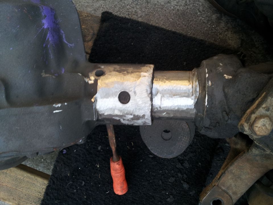 Close-up of a metal axle housing that has been cut and welded, with a chisel resting on it