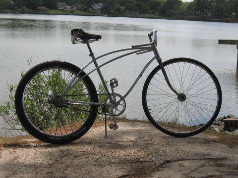 1994 Ford Bronco - A custom cruiser bicycle sits on a sandy shore next to a calm body of water.