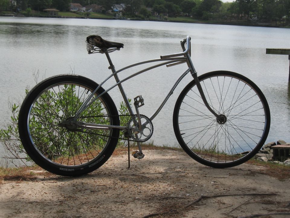 Silver cruiser bicycle with a sprung seat and wide tires parked by a lake