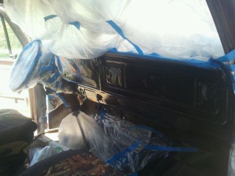 1979 Ford Bronco - The interior of a vehicle is being prepped for painting, with plastic sheeting and blue tape covering most surfaces.