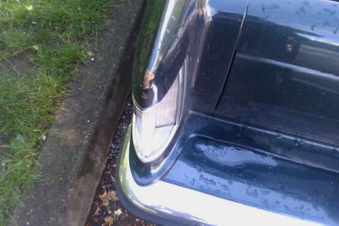 1991 Ford LTD Crown Victoria - A dark sedan's rear corner is visible, a chrome bumper and taillight with some rust.
