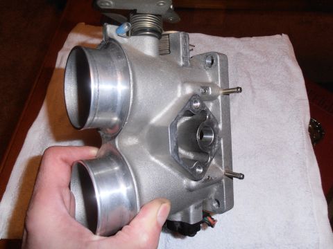 1990 Ford Bronco - A metal throttle body part is shown from a close-up angle, held by a hand against a white cloth.